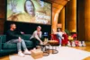 Talkrunde mit drei Männern auf Bühne, Florian Sump am Mikrofon, Leinwand mit Deine-Freunde-Motiv und Tonies-Figuren im Vordergrund