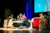 Zwei Podcaster beim Live-Event der KidsDoc-Tour auf Bühne mit grüner Couch, rotem Sessel und Deko zur 200. Folge