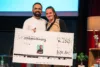 Dr. Vitor Gatinho und eine Frau präsentieren auf der Bühne einen kids.doc Spendenscheck über 250 Euro während der Tour.
